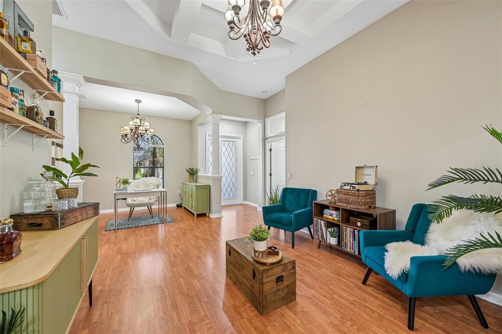 A living room and office area with wood floors, teal armchairs, and two chandeliers — 259 DAHLIA COURT, BRADENTON, FL