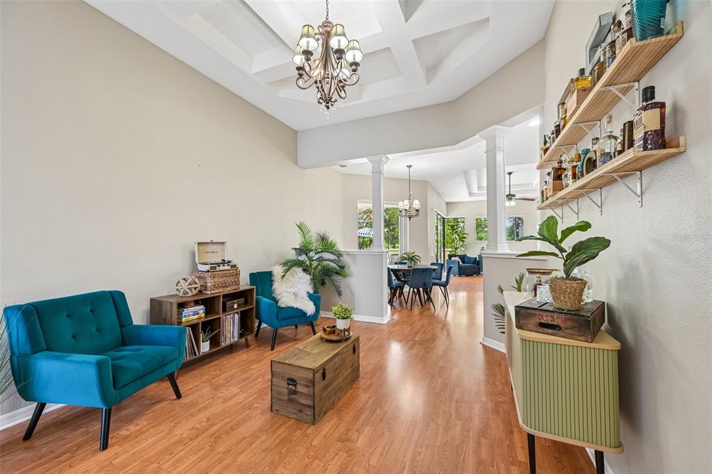 A living area features teal armchairs, wood flooring, a coffered ceiling, and wall-mounted shelving — 259 DAHLIA COURT, BRADENTON, FL