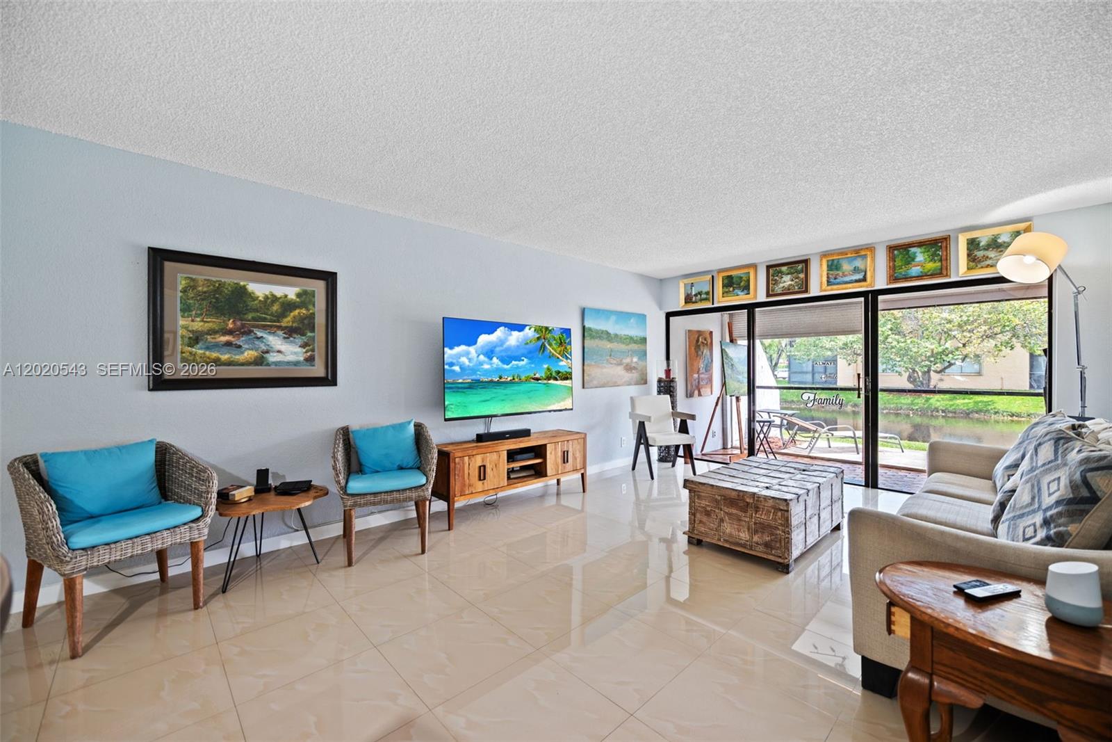 A living room features light blue walls, tile flooring, a television, and a sliding glass door — 200 Lakeview Dr # 113, Weston FL 33326, WESTON, FL