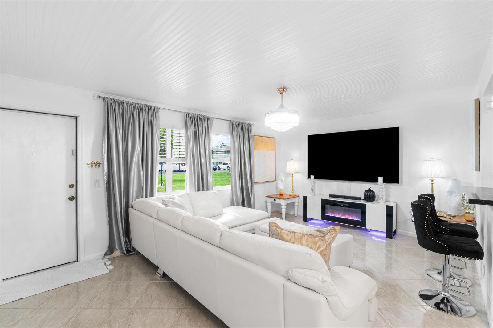 A bright living room features a white sectional sofa, a wall-mounted television, and tile flooring — 340 Horizons W # 102, Boynton Beach FL 33435, BOYNTON BEACH, FL