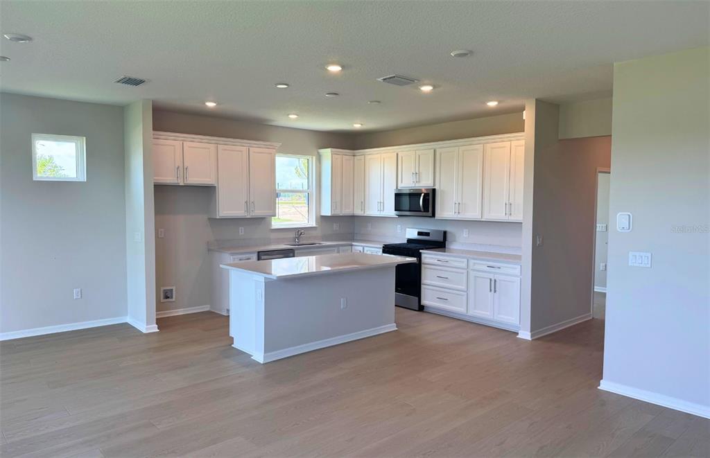 A modern kitchen features white cabinetry, a central island, and light-colored wood flooring — 9118 SERENADE DRIVE, MELBOURNE, FL