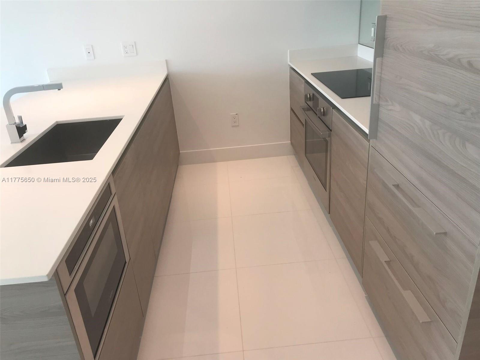 A modern galley kitchen features light wood cabinetry, white countertops, and stainless steel appliances — 1300 S MIAMI AVE # 4003, Miami FL 33130, MIAMI, FL