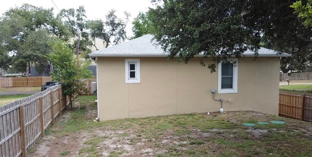 The exterior side view of a tan stucco house features two windows and a fence — 3225 LAUREL AVENUE, CLEARWATER, FL