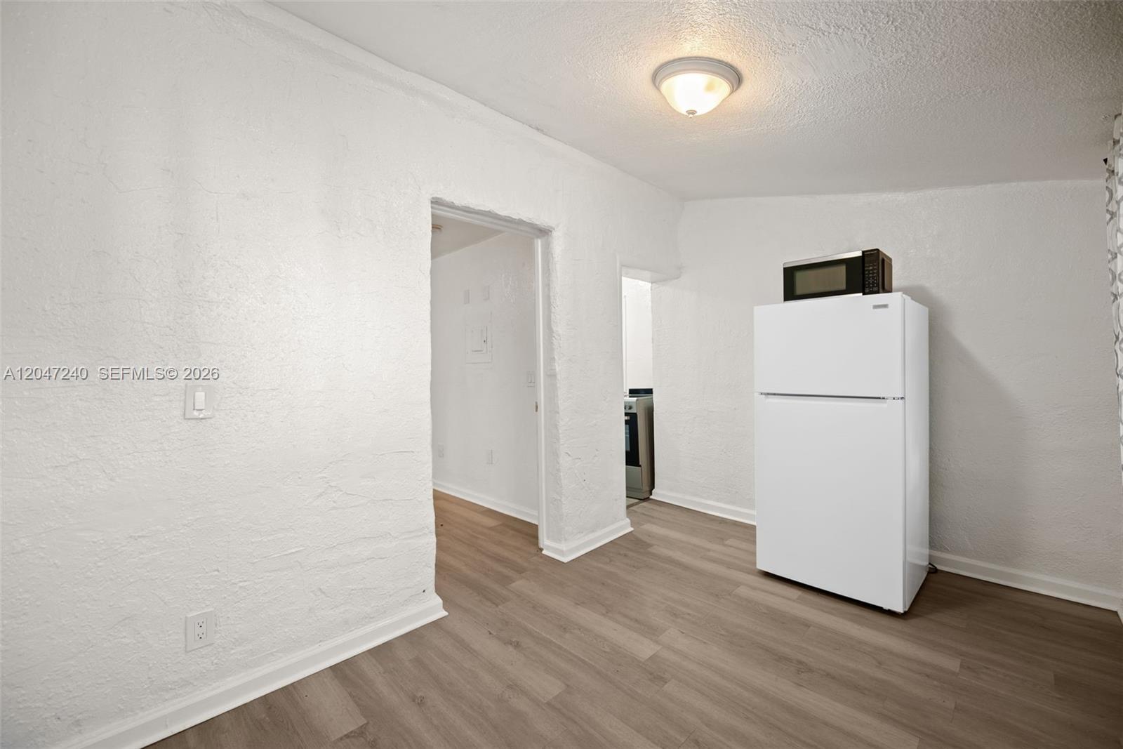 A white refrigerator stands in a room with textured white walls and wood-look flooring — MIAMI, FL