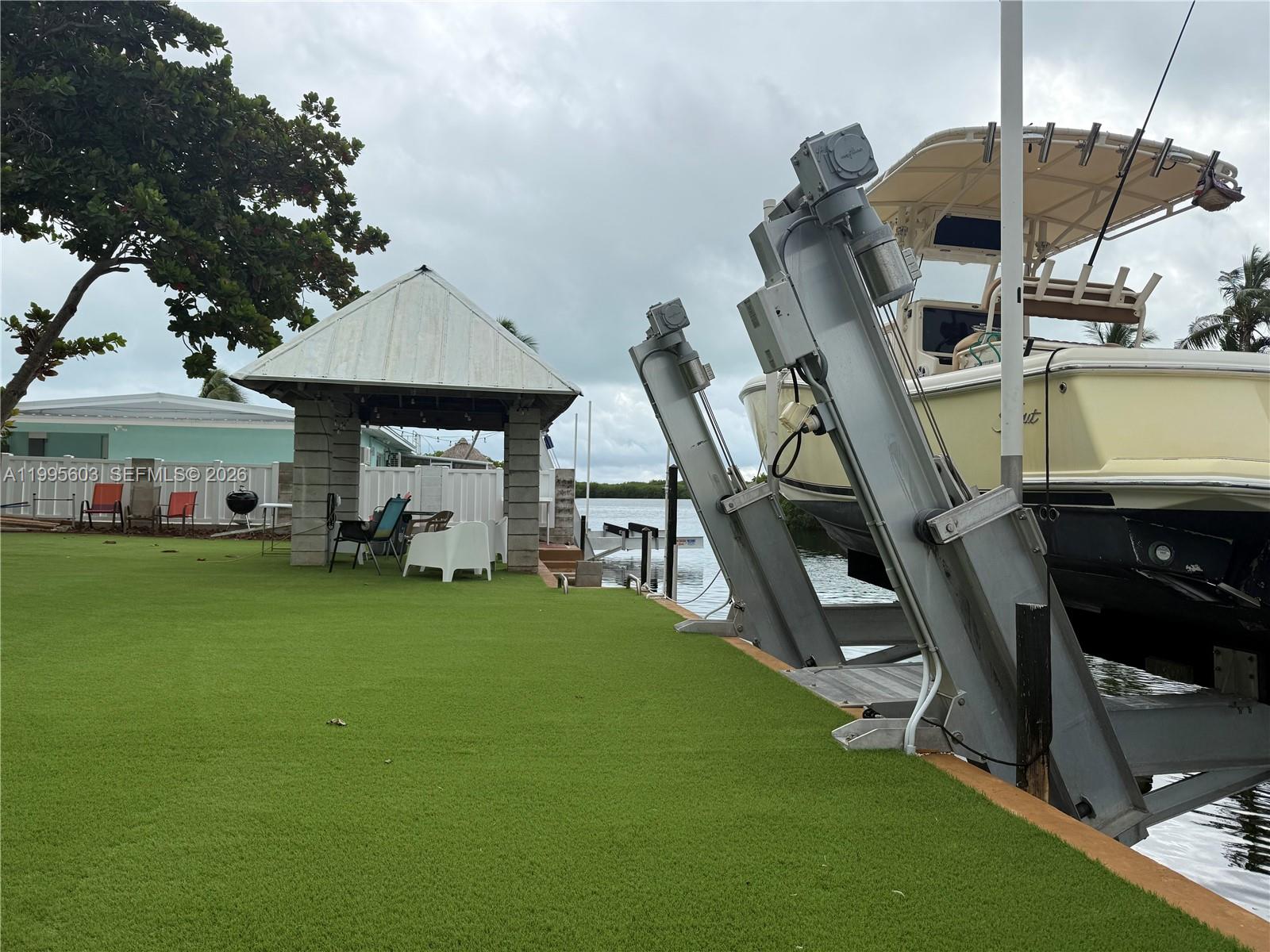 A boat lift sits beside a grassy lawn and a covered patio area — 1126 Grand St, Key Largo FL 33037, KEY LARGO, FL