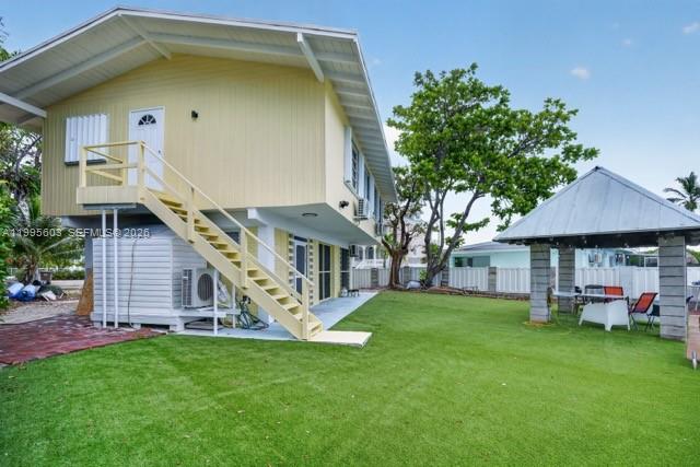 A two-story yellow house with an exterior staircase stands next to a covered patio — 1126 Grand St, Key Largo FL 33037, KEY LARGO, FL