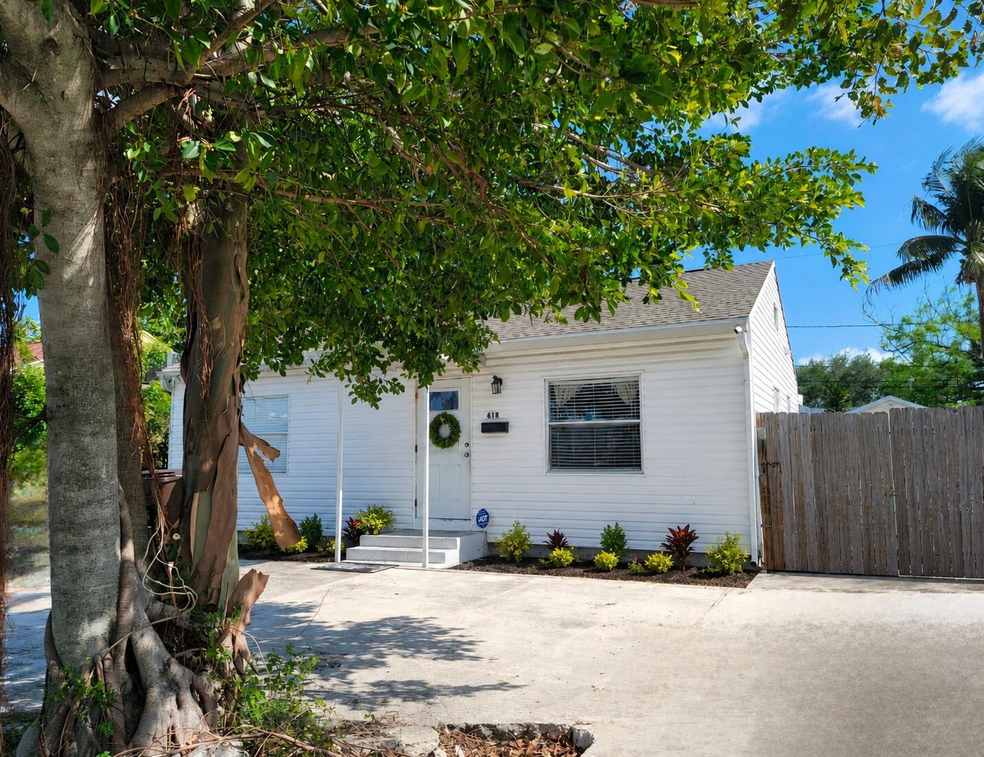 A white single-story house with a concrete driveway and a large tree in the foreground — 618 Hunter Street, West Palm Beach FL 33405, WEST PALM BEACH, FL