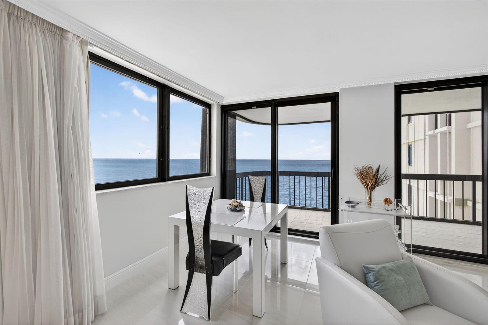 A dining area features a white table, modern chairs, and large windows overlooking the ocean — 5380 N Ocean Drive # 12e, Singer Island FL 33404, SINGER ISLAND, FL
