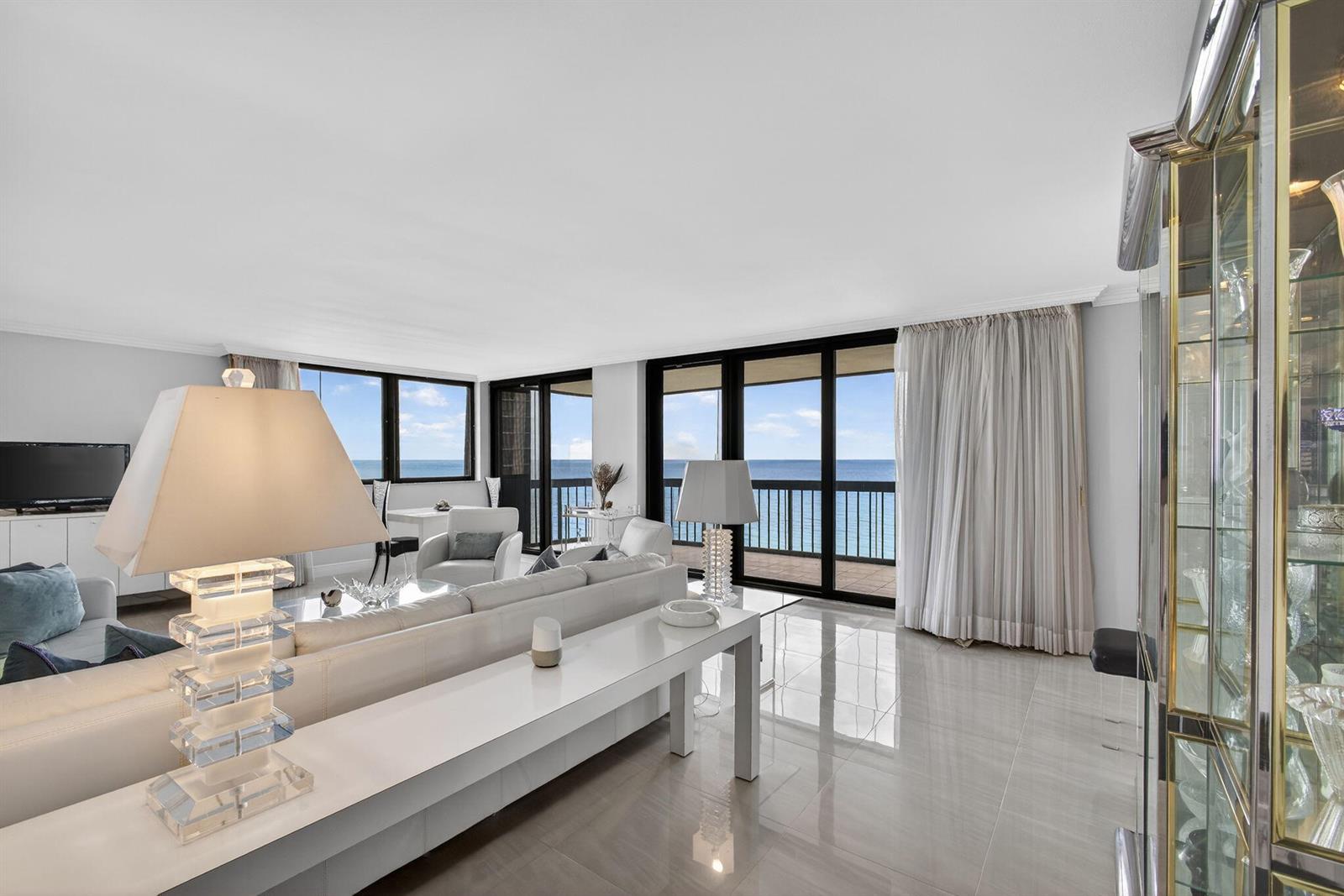 A bright living room features white tile floors, a glass-topped console table, and ocean views — 5380 N Ocean Drive # 12e, Singer Island FL 33404, SINGER ISLAND, FL