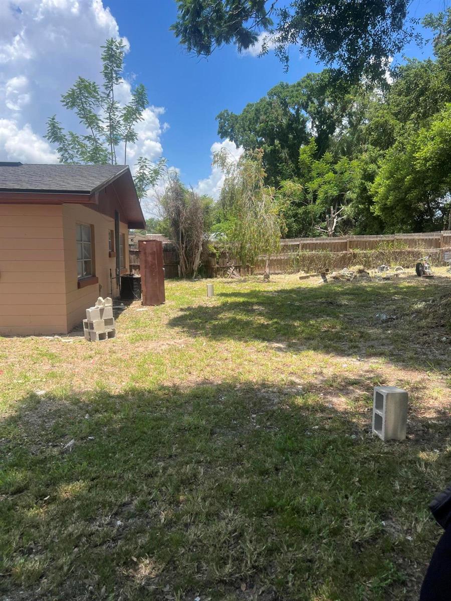 A view of a backyard with a tan house, sparse grass, and a wooden fence — 1858 4th Street SE, Winter Haven FL 33880, WINTER HAVEN, FL