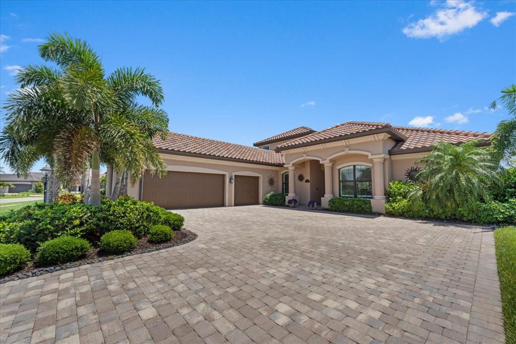 A single-story house with a tiled roof and paver driveway under a vibrant sunset sky — 5580 MULLIGAN WAY, LAKEWOOD RANCH, FL