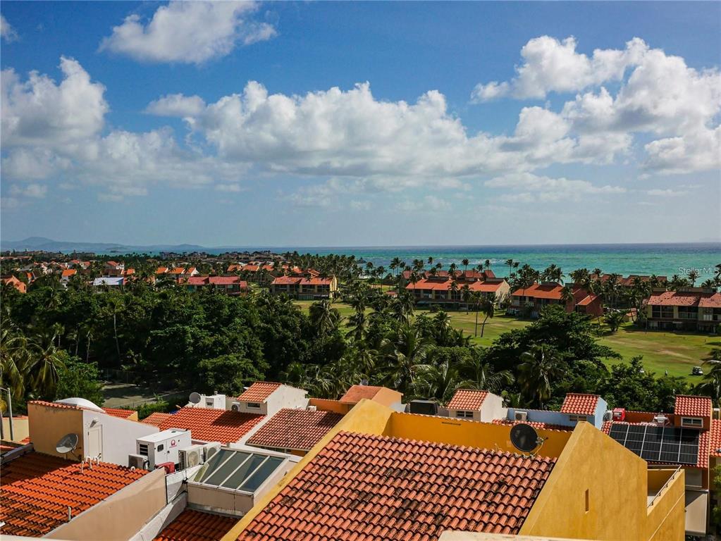 An elevated view of a coastal resort with red-tiled roofs, palm trees, and the ocean — 285 PALMAS INN DRIVE UNIT 8-302, HUMACAO, PR