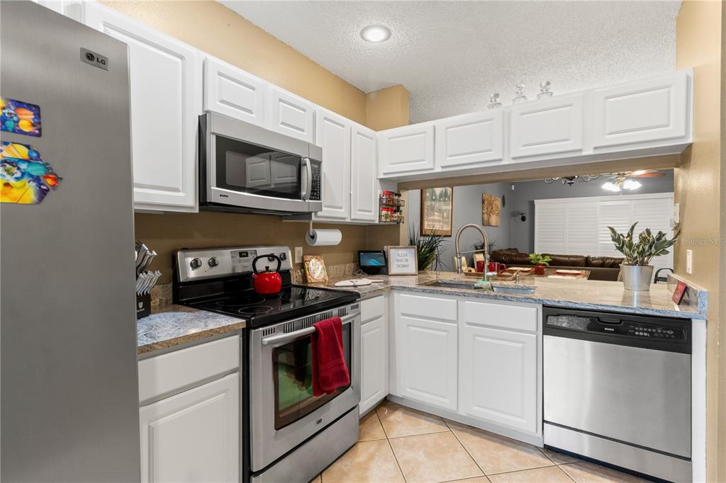 A kitchen with white cabinets, stainless steel appliances, and a pass-through window to the living area — 8635 HUNTERS KEY CIRCLE, TAMPA, FL