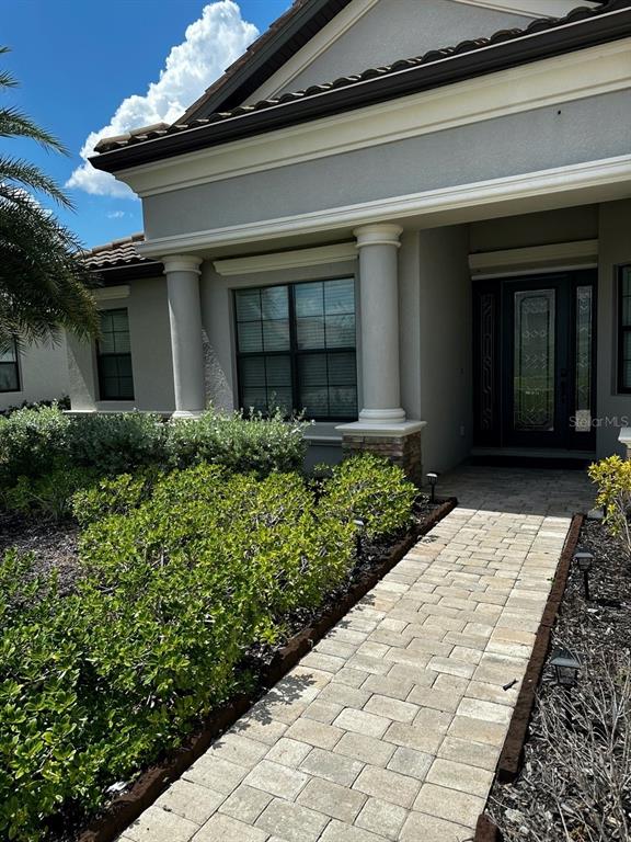 A paved walkway leads to the front entrance of a house with columns and landscaping — 17025 POLO TRAIL, BRADENTON, FL