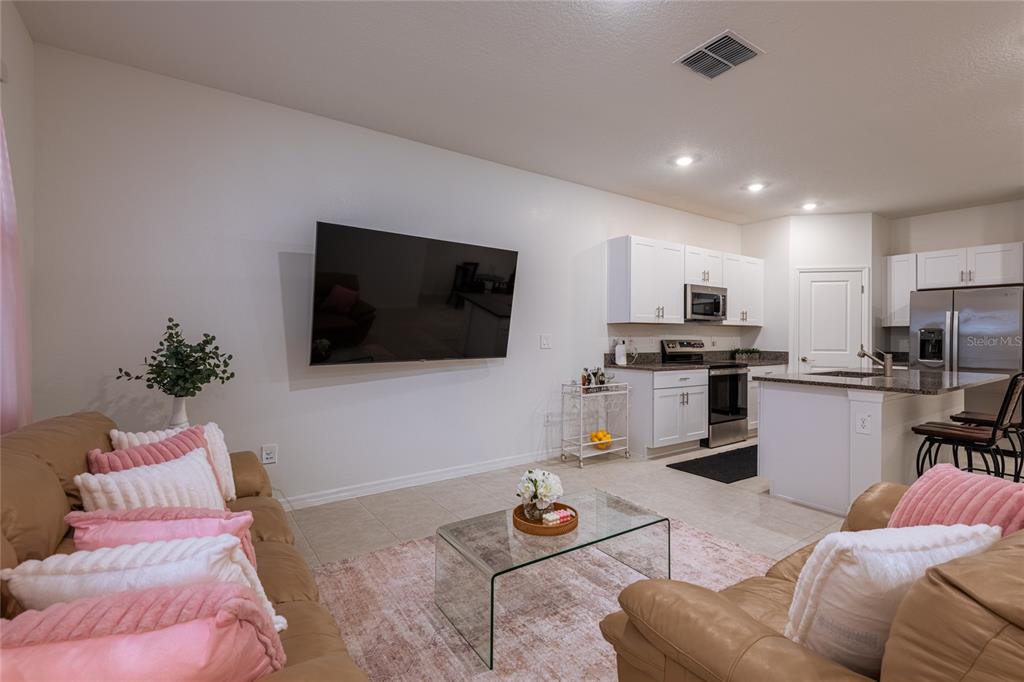 An open-concept living room and kitchen featuring tan leather sofas, a glass coffee table, and white cabinetry — 10807 E FORT WHITE COURT, TAMPA, FL