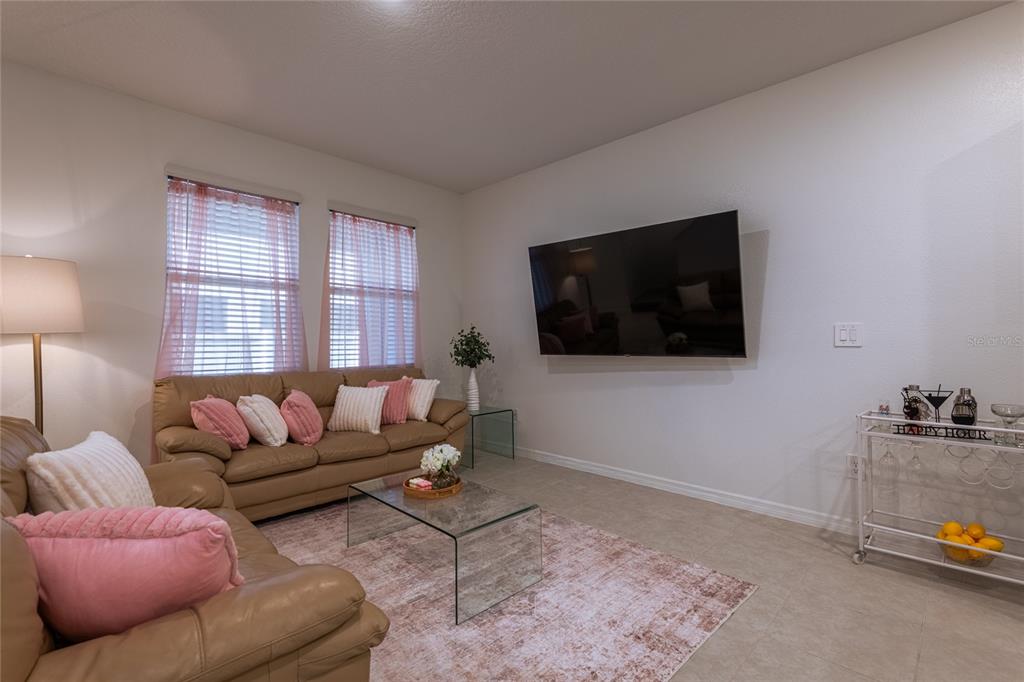 A living room features a tan leather sofa, a glass coffee table, and a wall-mounted television — 10807 E FORT WHITE COURT, TAMPA, FL