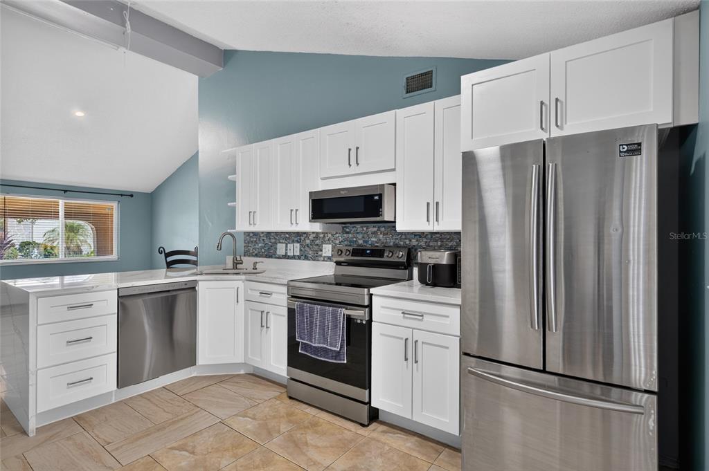 A kitchen features white cabinets, stainless steel appliances, a blue tiled backsplash, and tile flooring — 6711 GLEN FOREST COURT, TAMPA, FL