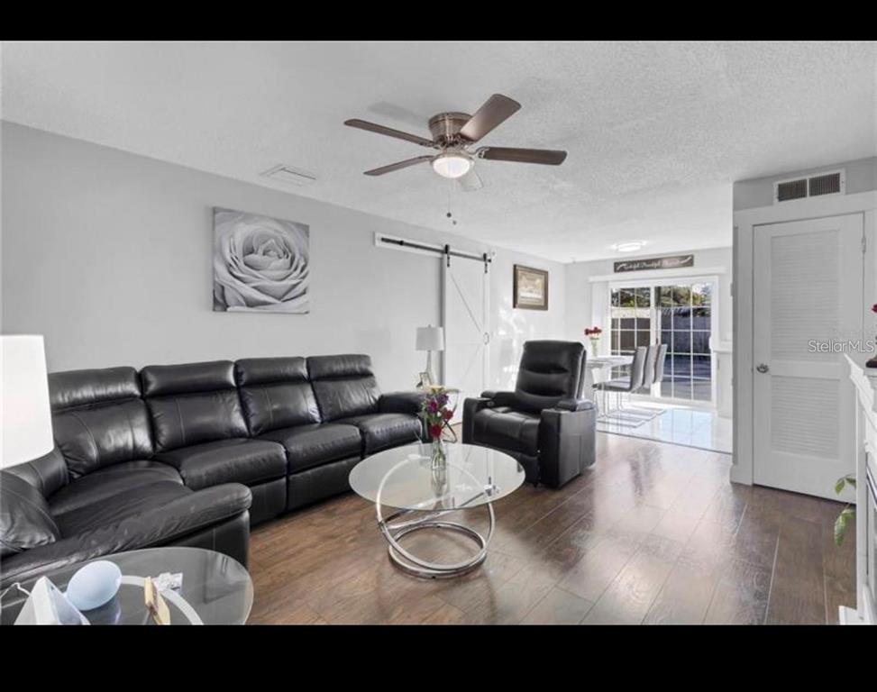 A living room with dark leather furniture, a glass coffee table, and wood-look flooring — 314 W GROSSENBACHER DRIVE, APOPKA, FL