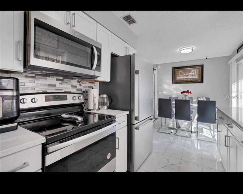 A modern kitchen with white cabinets, stainless steel appliances, and an adjacent dining area — 314 W GROSSENBACHER DRIVE, APOPKA, FL