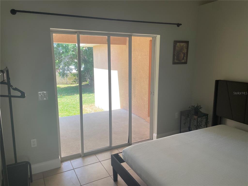 A bedroom features tile flooring, a bed, and sliding glass doors leading to a patio — 1216 ALAMEDA DRIVE N, LAKELAND, FL