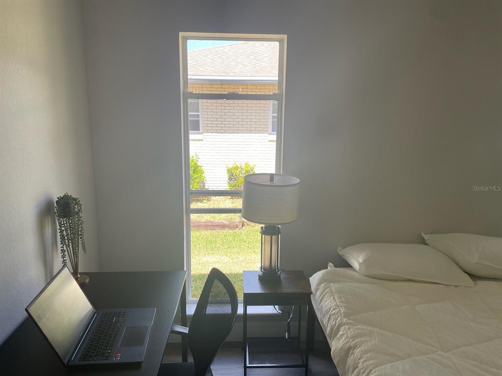 A bedroom features a desk with a laptop, a window, a nightstand with a lamp, and a bed — 1216 ALAMEDA DRIVE N, LAKELAND, FL
