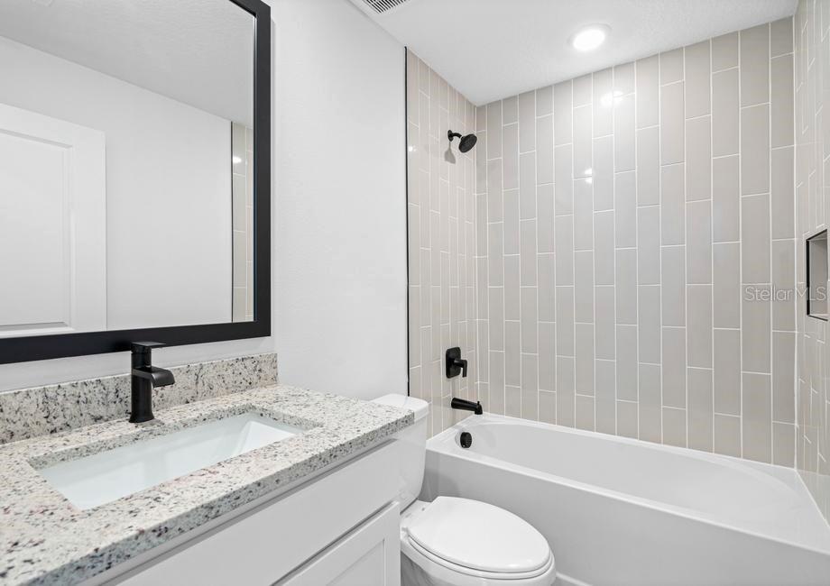 A bathroom features a granite vanity, a black faucet, and a tub with tiled walls — 657 BLACKTHORN DRIVE, LAKELAND, FL