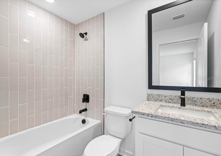 A bathroom featuring a bathtub with light pink tile walls, a toilet, and a vanity — 657 BLACKTHORN DRIVE, LAKELAND, FL