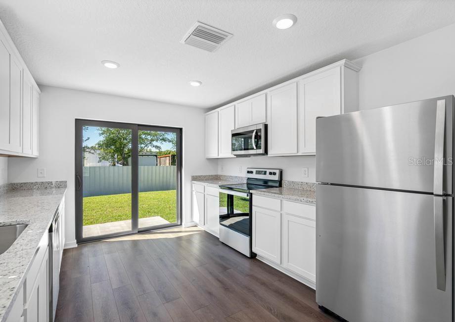 A kitchen with white cabinets, granite countertops, stainless steel appliances, and a sliding glass door — 657 BLACKTHORN DRIVE, LAKELAND, FL