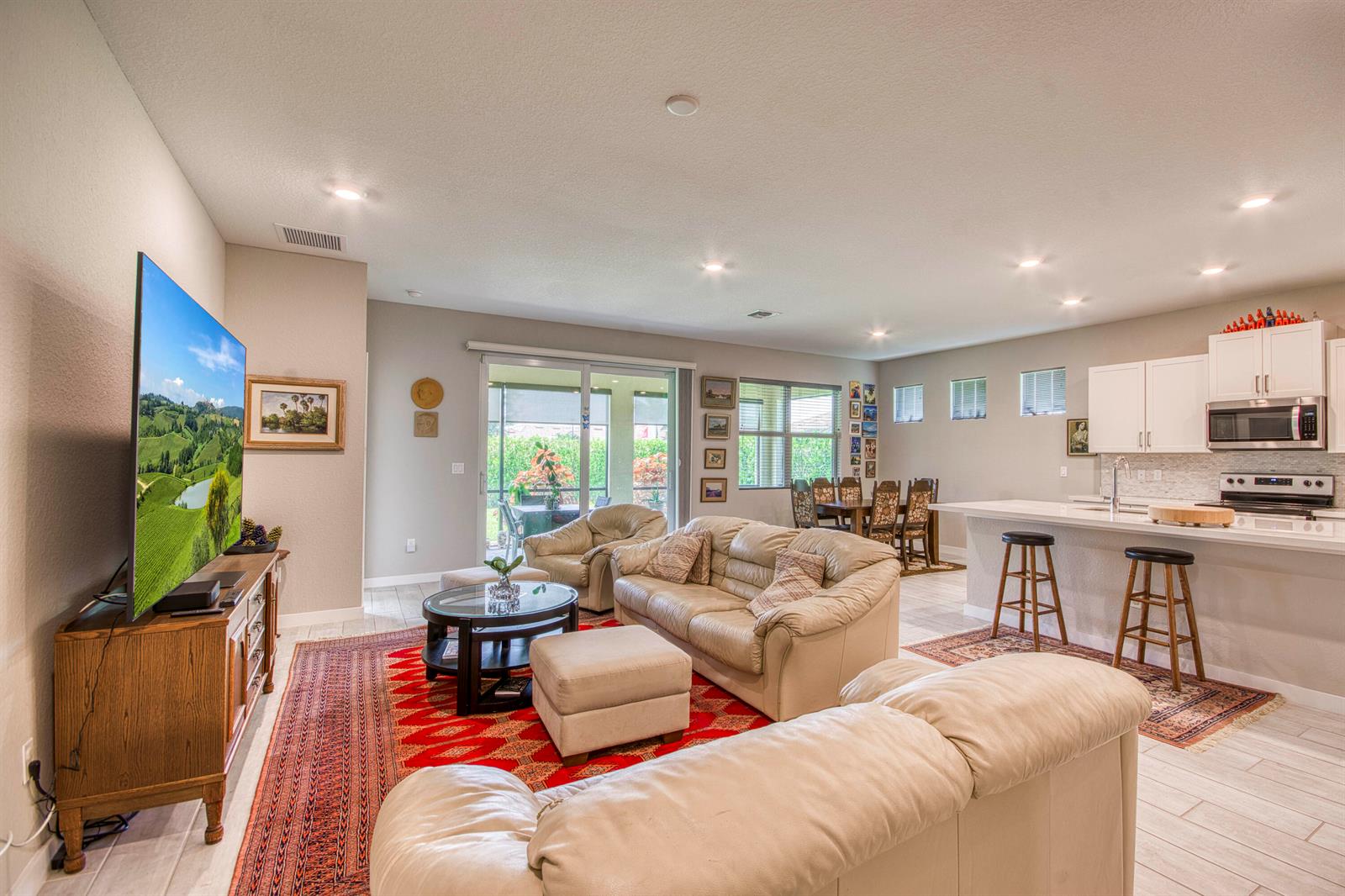 An open-concept living room and kitchen feature light tile floors, leather furniture, and area rugs — 4720 NW Exchange Avenue, Jensen Beach FL 34957, JENSEN BEACH, FL