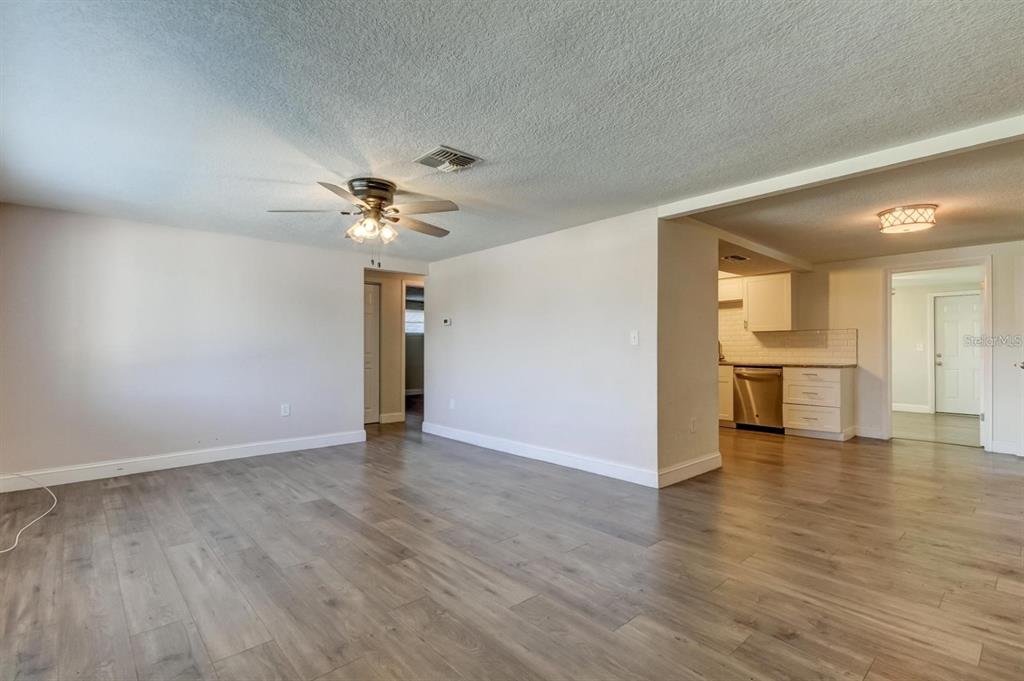 A living room with light wood-look flooring, a ceiling fan, and an adjacent kitchen area — 7144 FAIRFAX DRIVE, PORT RICHEY, FL