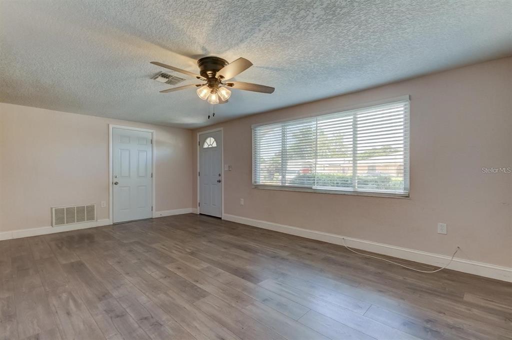 An empty room with light-colored walls, wood-look flooring, a ceiling fan, and a large window — 7144 FAIRFAX DRIVE, PORT RICHEY, FL