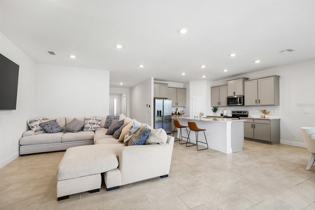 An open-concept living room and kitchen featuring light tile floors and gray cabinetry — 5689 HAWKS CAY STREET, APOLLO BEACH, FL