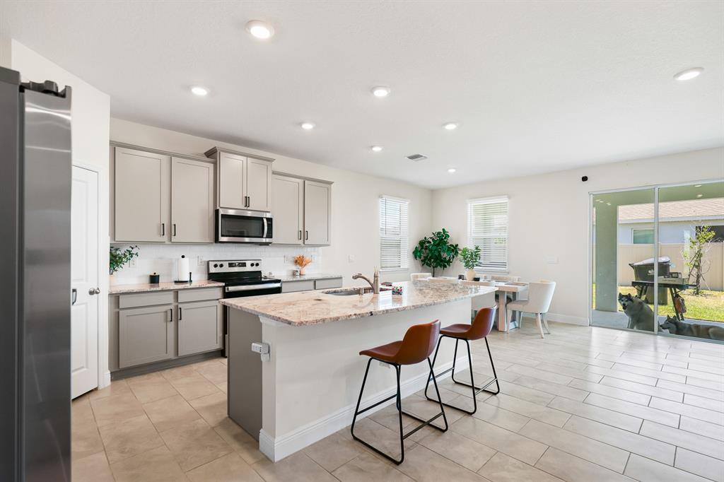 A kitchen with gray cabinets, granite countertops, an island with two stools, and a dining area — 5689 HAWKS CAY STREET, APOLLO BEACH, FL