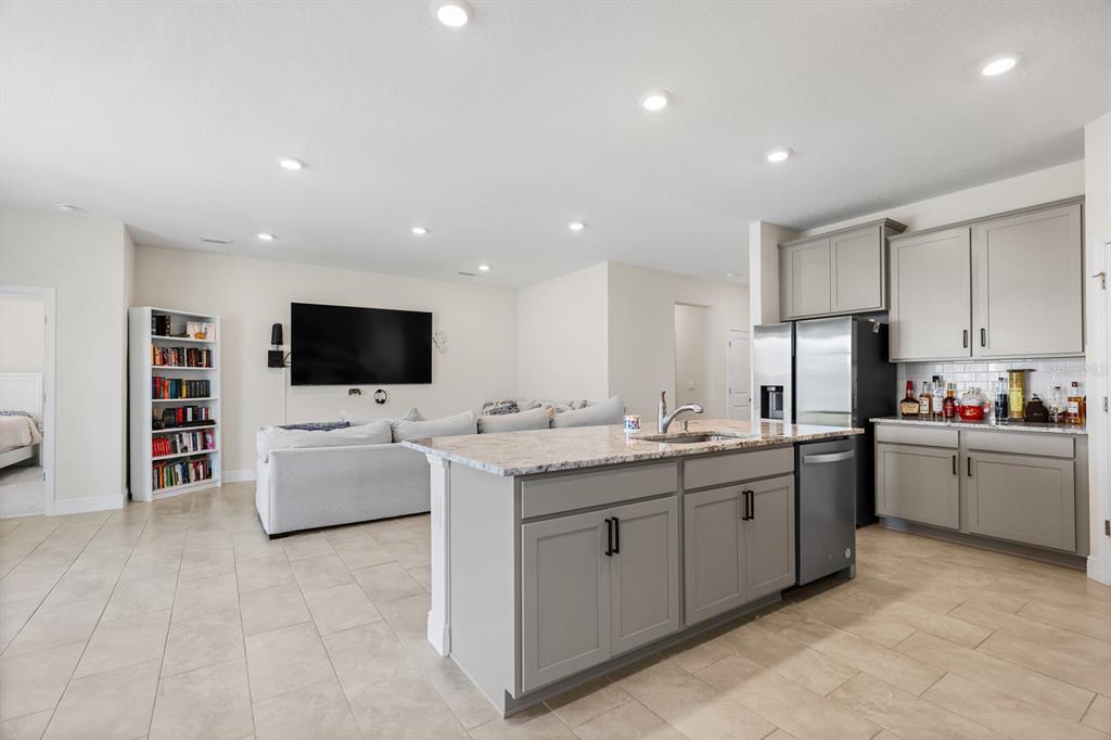 A kitchen with a granite-topped island and gray cabinets overlooks a living room area — 5689 HAWKS CAY STREET, APOLLO BEACH, FL