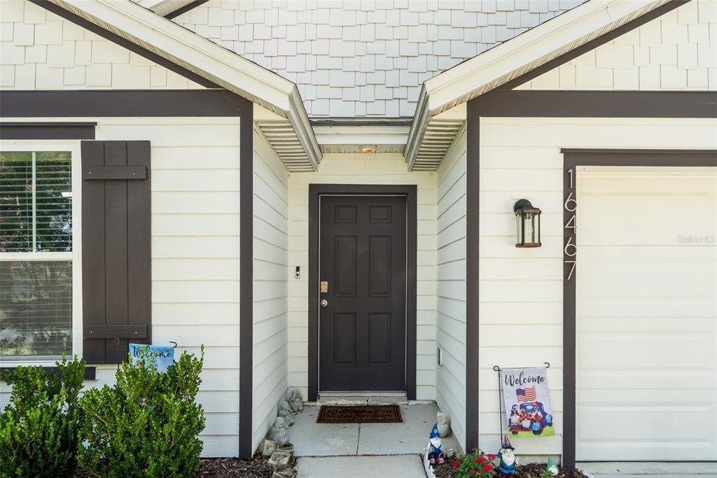 A front entryway features a dark door, white siding, a garage, and decorative garden gnomes — 16467 NW 192ND TERRACE, HIGH SPRINGS, FL