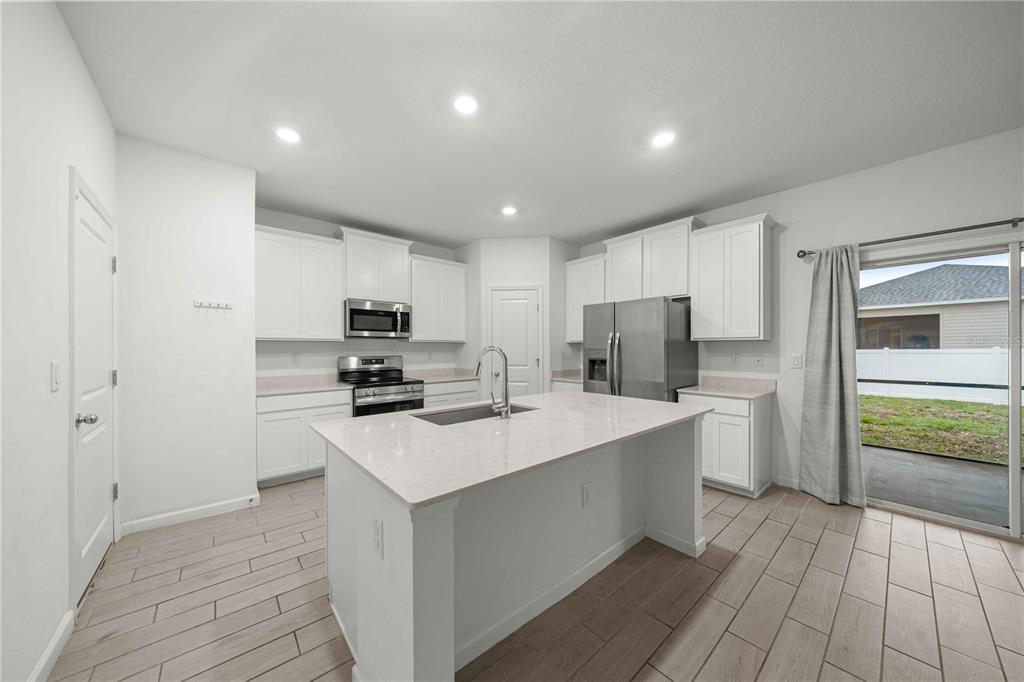 A modern kitchen features white cabinets, a central island with a sink, and tile flooring — 3980 NE 34TH AVENUE, OCALA, FL