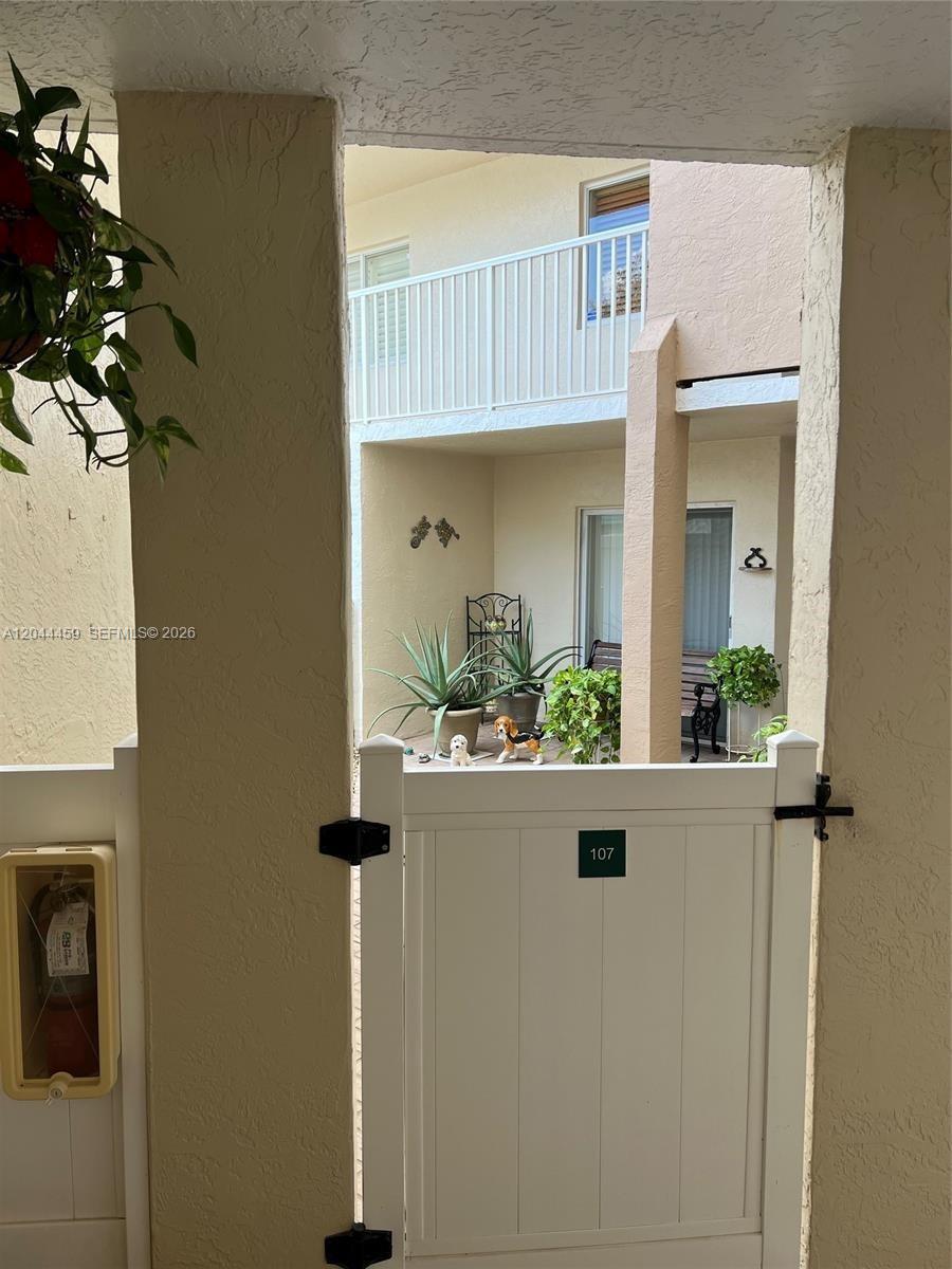 A white gate with the number 107 leads to a small patio with potted plants — 9551 Weldon Cir # E107, Tamarac FL 33321, TAMARAC, FL