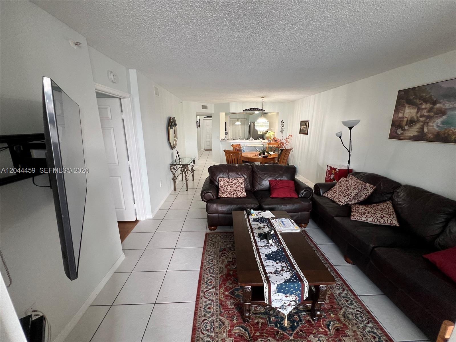 A living room with tile floors, leather sofas, and a dining area in the background — 9551 Weldon Cir # E107, Tamarac FL 33321, TAMARAC, FL