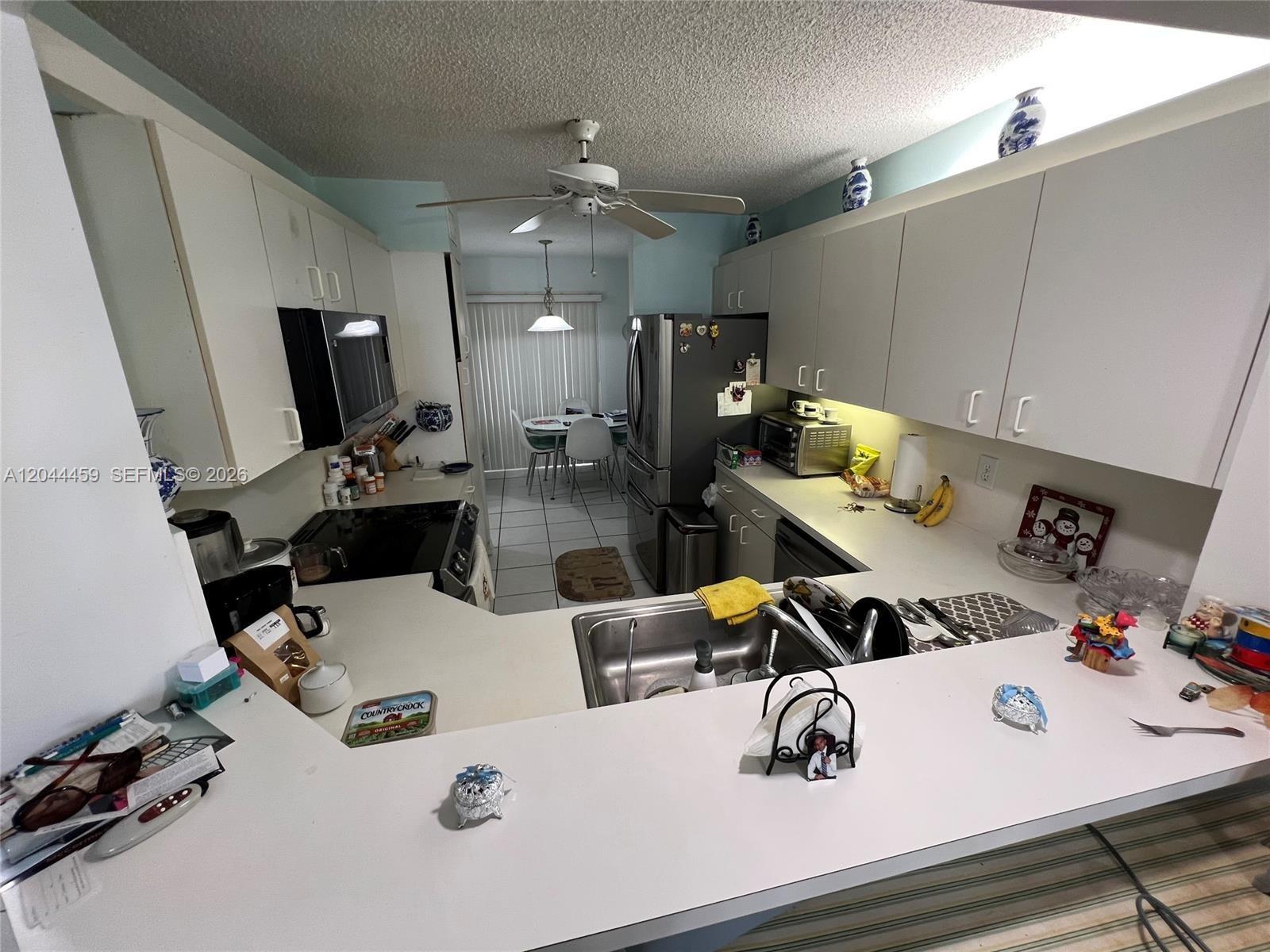 A kitchen features white cabinets, a peninsula countertop, and a dining area with sliding doors — 9551 Weldon Cir # E107, Tamarac FL 33321, TAMARAC, FL
