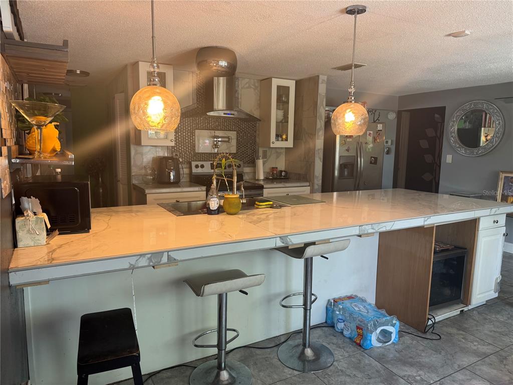 A kitchen features a large marble-topped island with bar stools and pendant lighting — 10424 CHOICE DRIVE, PORT RICHEY, FL