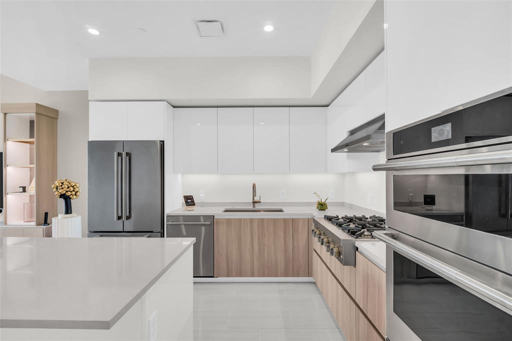 A modern kitchen features white upper cabinets, wood-tone lower cabinets, stainless steel appliances, and quartz countertops — 400 CENTRAL AVENUE UNIT 2705, ST PETERSBURG, FL