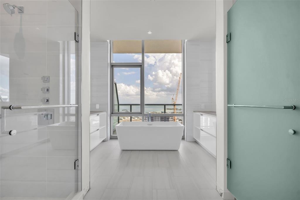 A modern bathroom features a freestanding tub, glass-enclosed shower, white cabinetry, and floor-to-ceiling windows — 400 CENTRAL AVENUE UNIT 2705, ST PETERSBURG, FL