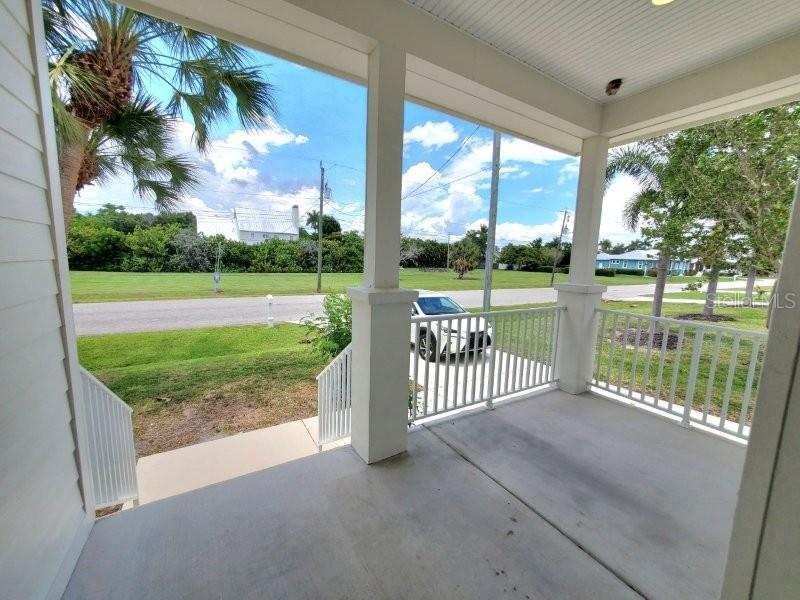A covered porch with white railings overlooks a grassy yard and a parked white car — 431 W MCKENZIE STREET, PUNTA GORDA, FL