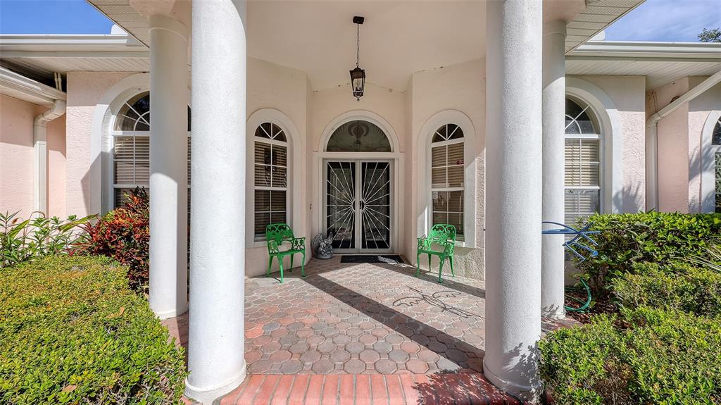 A covered front entryway features two large white columns, a paved patio, and green chairs — 7025 N SERENOA DRIVE, SARASOTA, FL