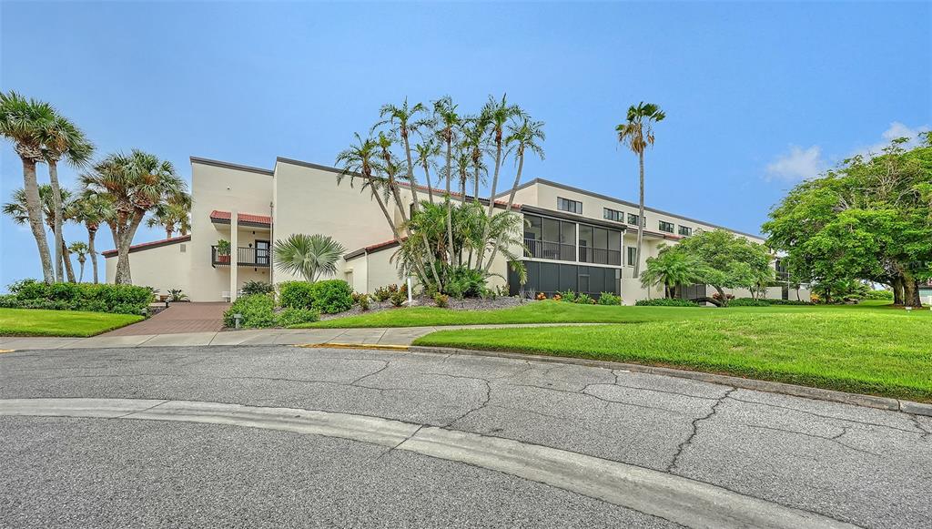 A multi-story beige building with screened balconies sits behind a lawn and palm trees — 2089 GULF OF MEXICO DRIVE UNIT G1-104, LONGBOAT KEY, FL