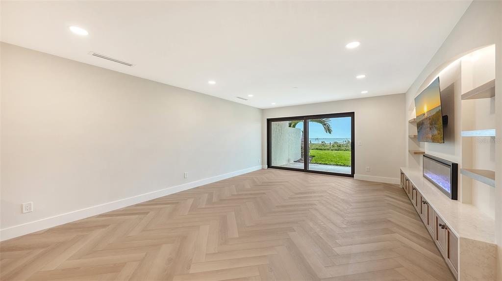 A living room features a fireplace, wall-mounted television, built-in shelving, and two beige sofas — 2089 GULF OF MEXICO DRIVE UNIT G1-104, LONGBOAT KEY, FL