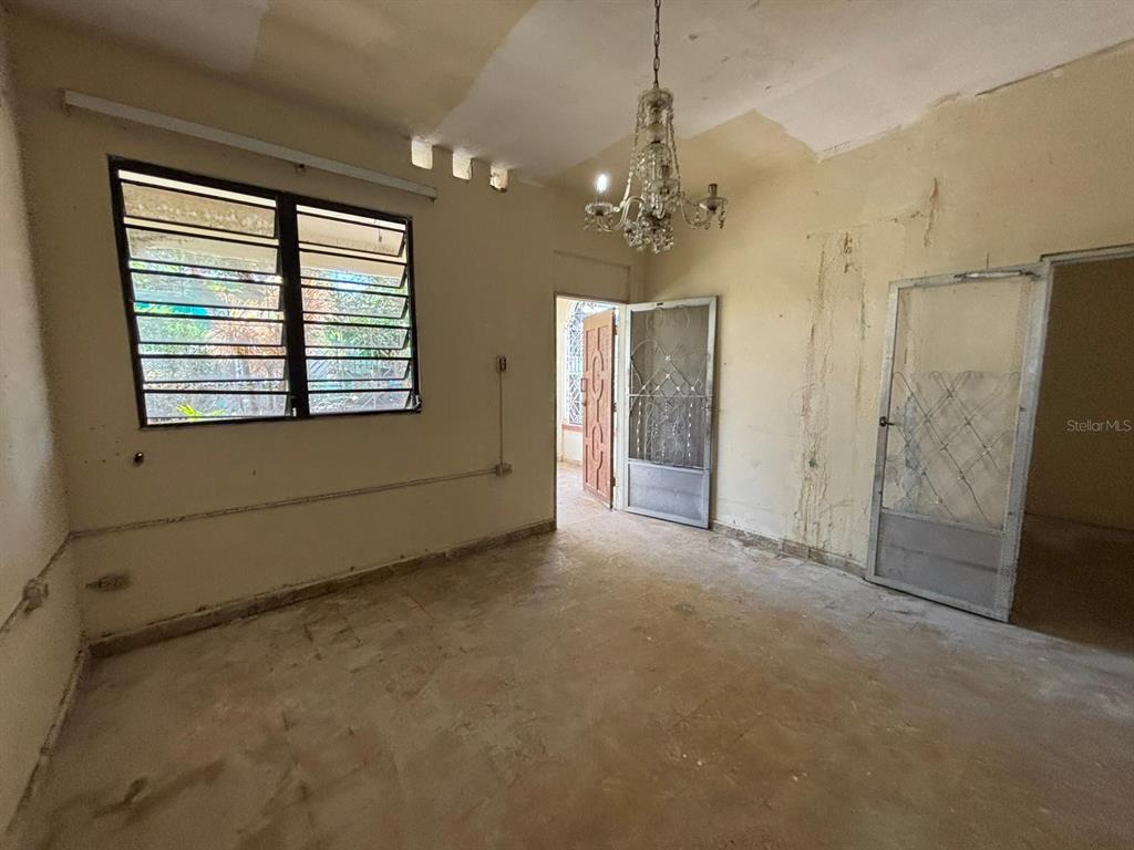 An empty room features a crystal chandelier, louvered windows, and unfinished walls and floors — D-13C Fajardo St. MIRAPALMERAS, SAN JUAN, PR