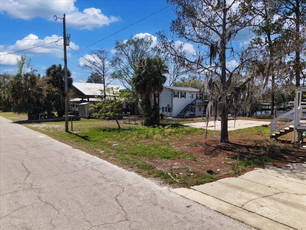 A vacant lot with a concrete pad, trees, and a neighboring house under a blue sky — 000 SE SE 241 STREET, OLD TOWN, FL