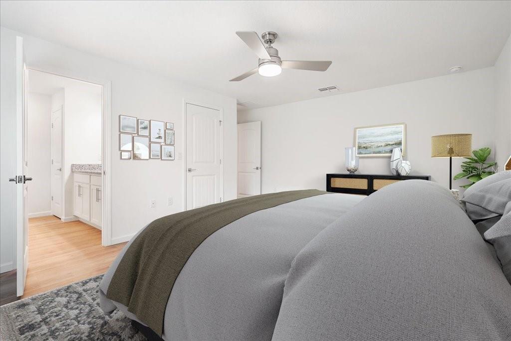 A bedroom features a gray bed, a ceiling fan, and an open door to a bathroom — 24 WOODSIDE DRIVE, PALM COAST, FL