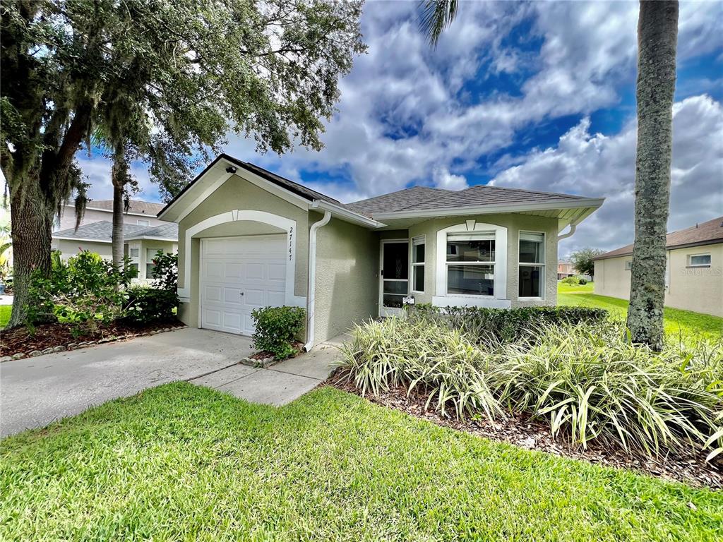 A single-story house with a white garage door, light green stucco siding, and a landscaped yard — 27147 BIG SUR DRIVE, WESLEY CHAPEL, FL